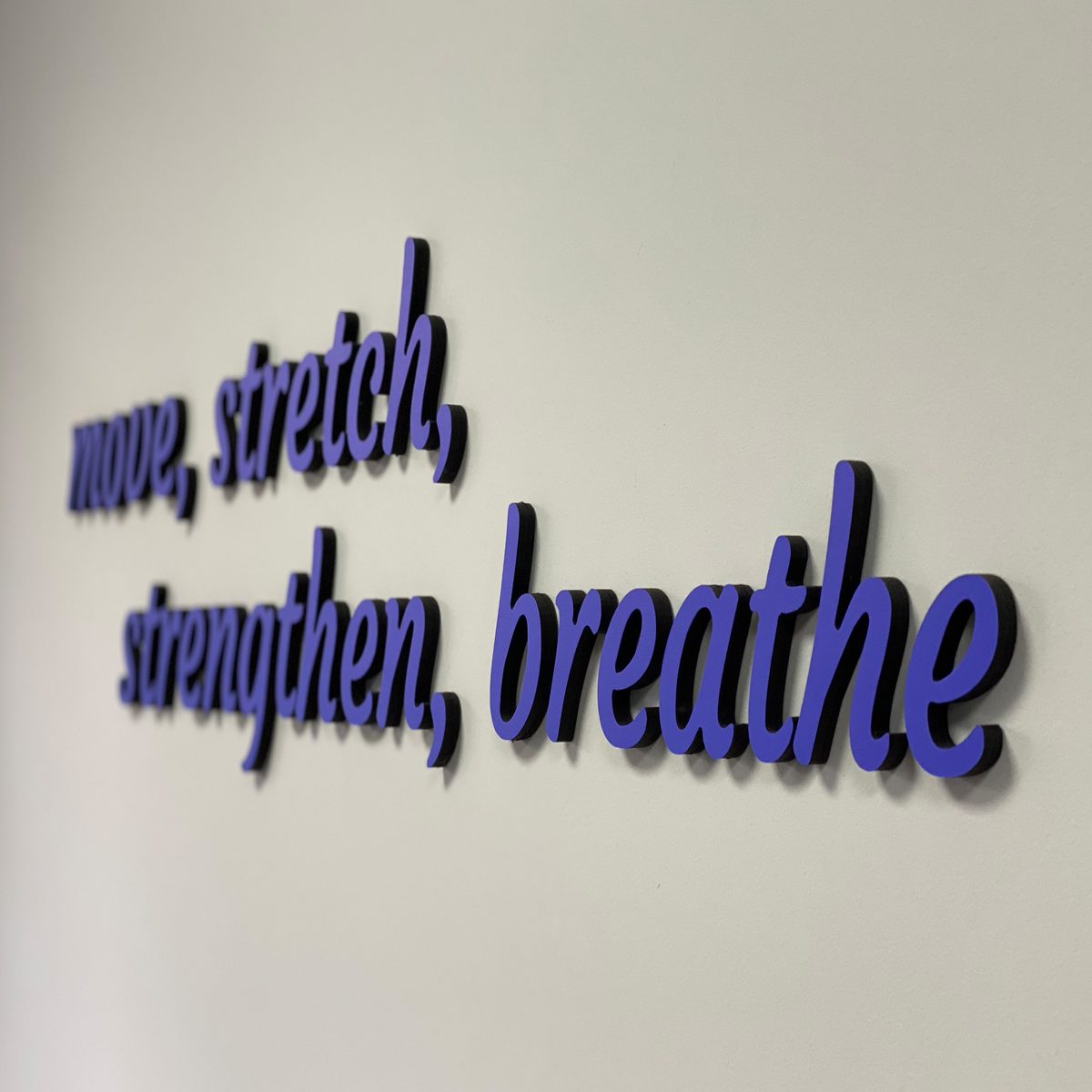 Purple 3D lettering reading 'move, stretch, strengthen, breathe' on a pale wall