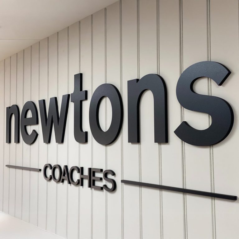 Black 3D 'newtons COACHES' lettering on a white vertical-panelled wall