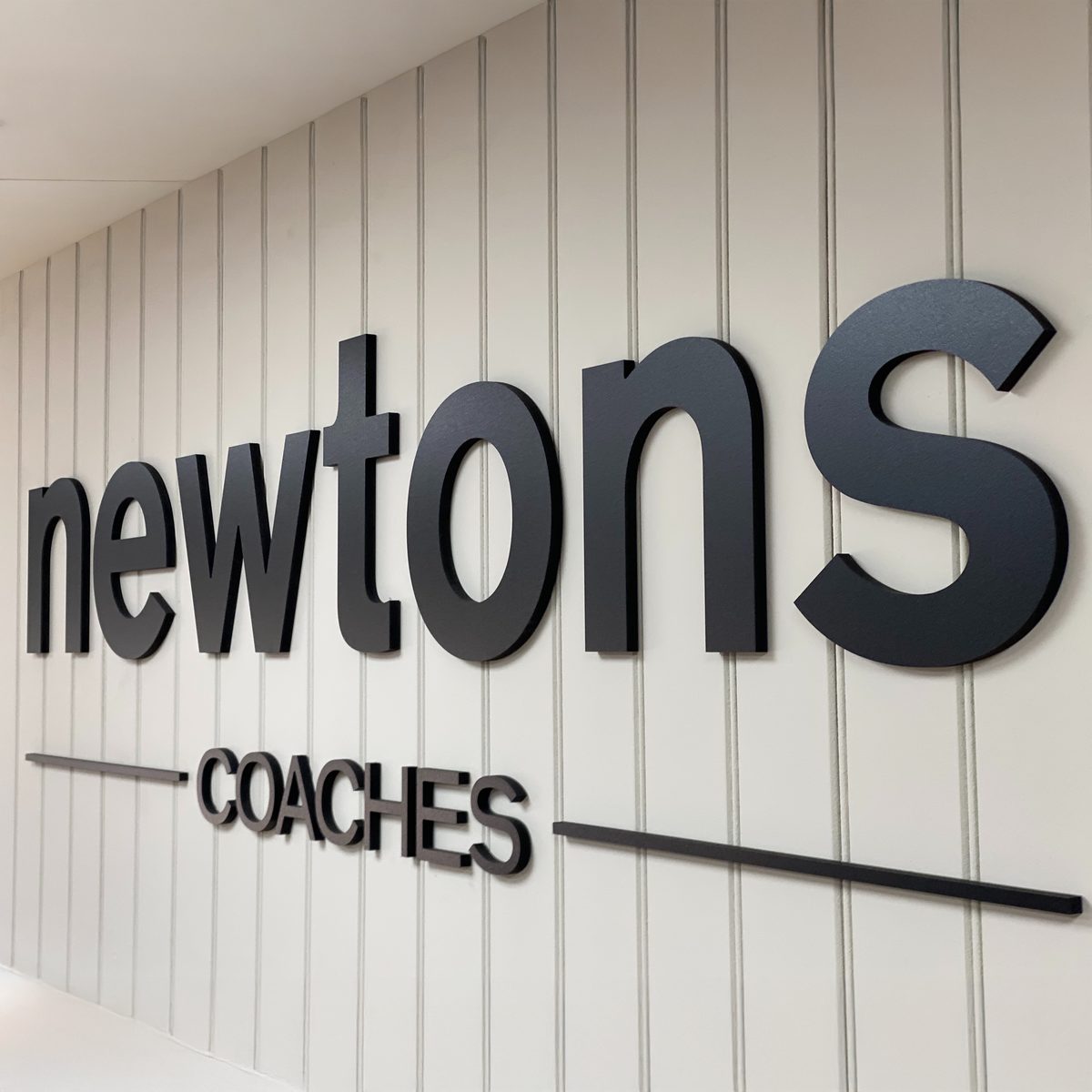 Black 3D 'newtons COACHES' lettering on a white vertical-panelled wall