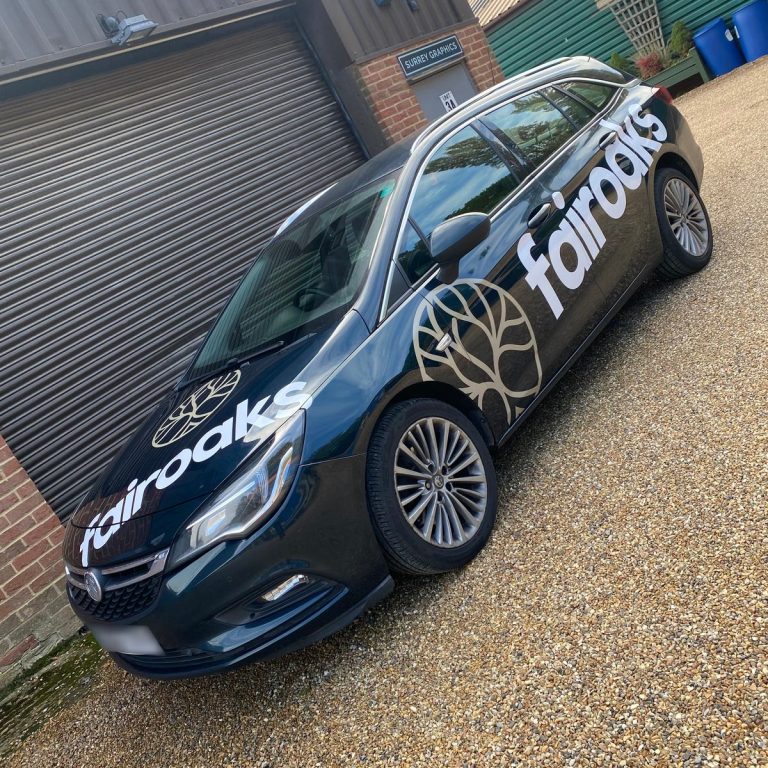 Dark estate car with white 'fairoaks' lettering and gold tree logo on bonnet and doors