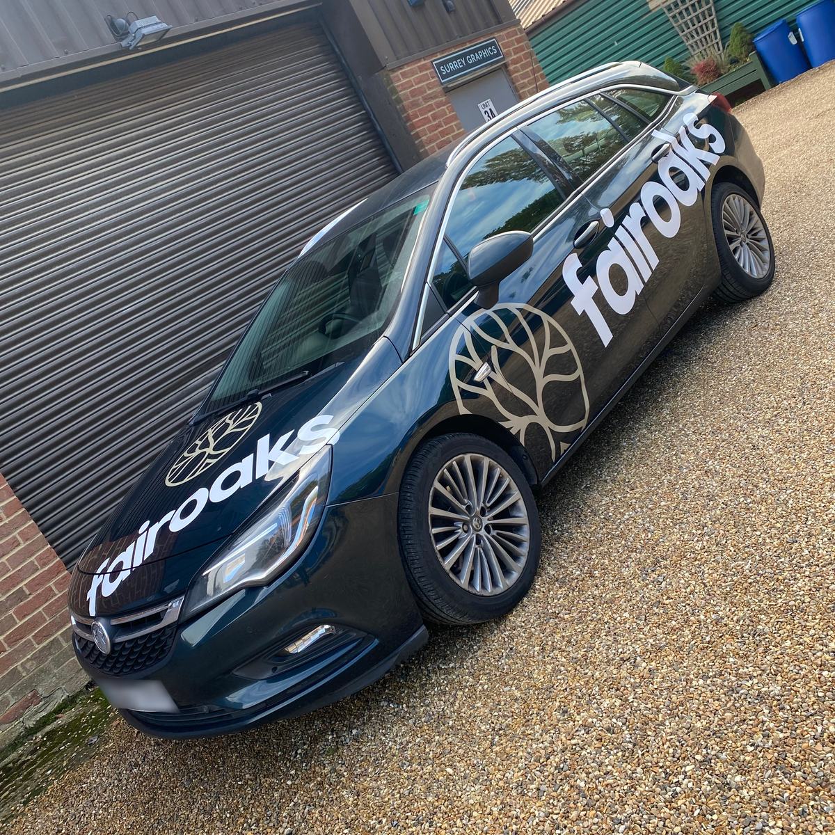 Dark estate car with white 'fairoaks' lettering and gold tree logo on bonnet and doors