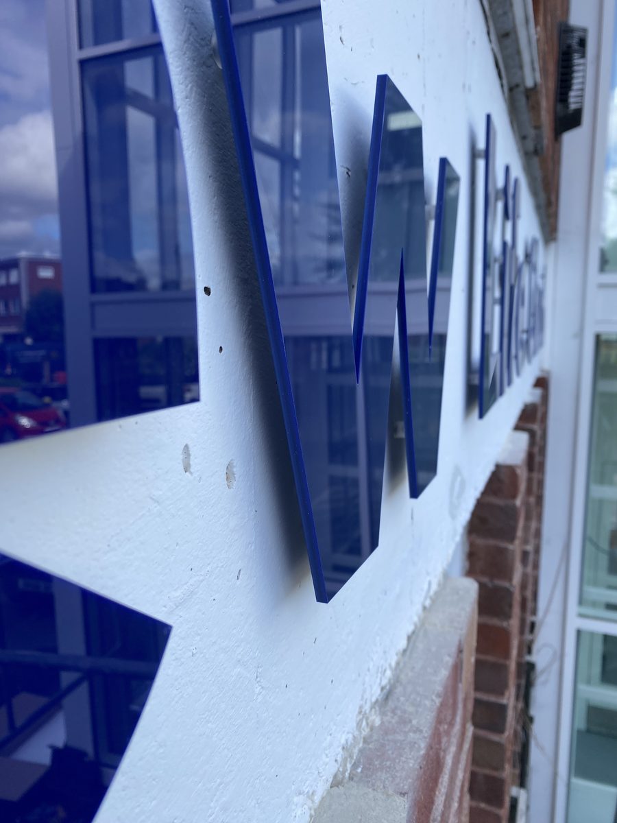 Close-up of blue acrylic letters on a white building fascia, shallow focus
