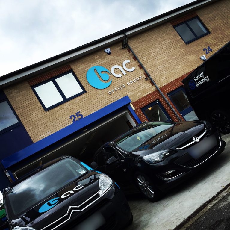 Blue and white 3D bac Office Group logo on a brick office unit, with branded cars parked outside
