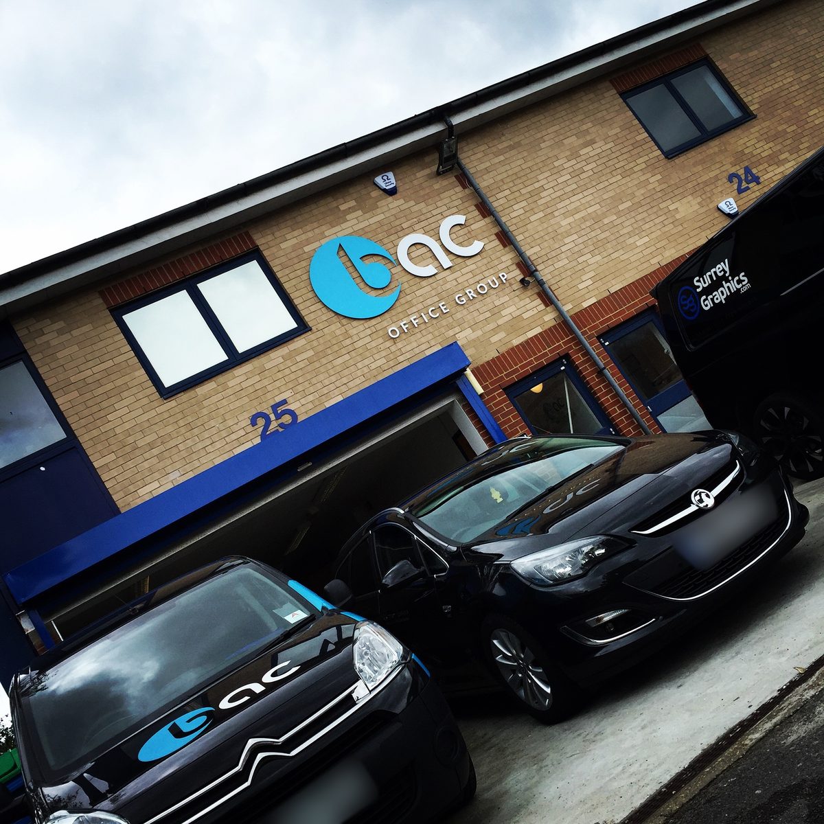 Blue and white 3D bac Office Group logo on a brick office unit, with branded cars parked outside