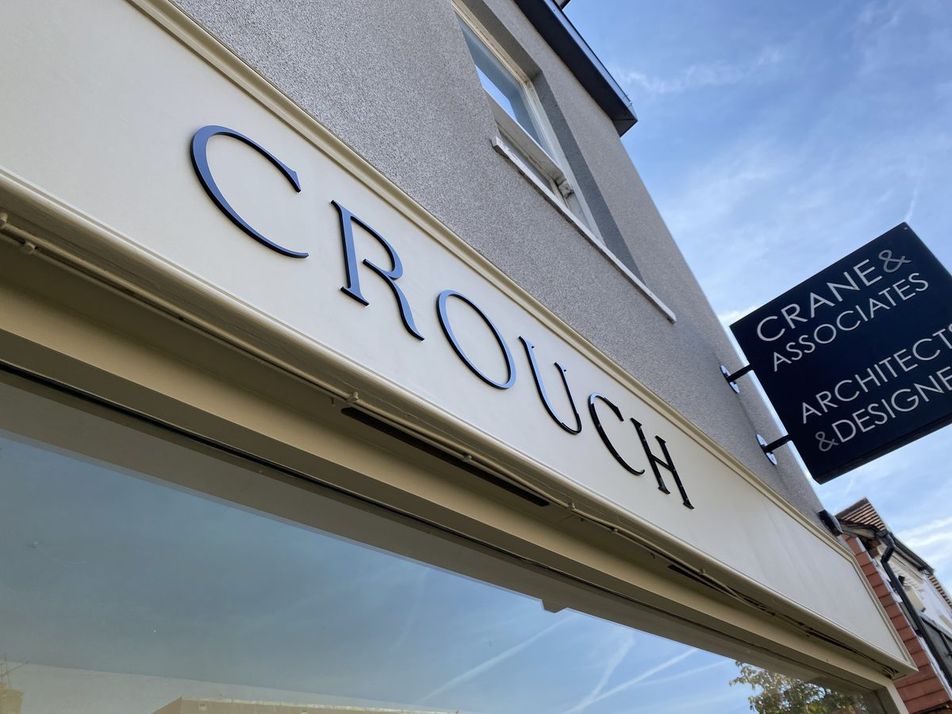 Dark 3D 'Crouch' letters on a cream fascia, viewed from below, with a hanging Crane & Associates sign