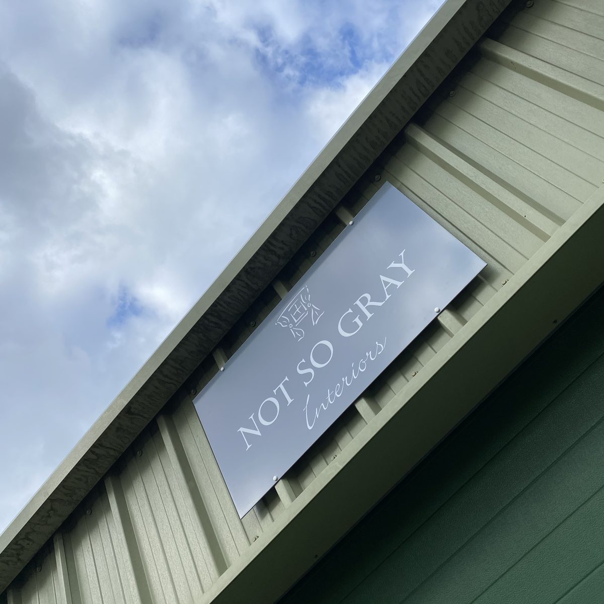 Grey 'Not So Gray Interiors' aluminium composite sign mounted on green timber cladding