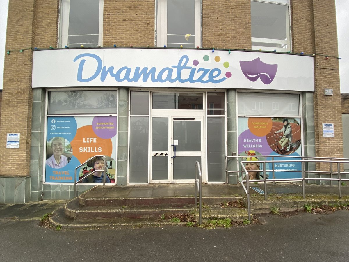 Dramatize white fascia sign with blue lettering and purple mask logo above a building entrance