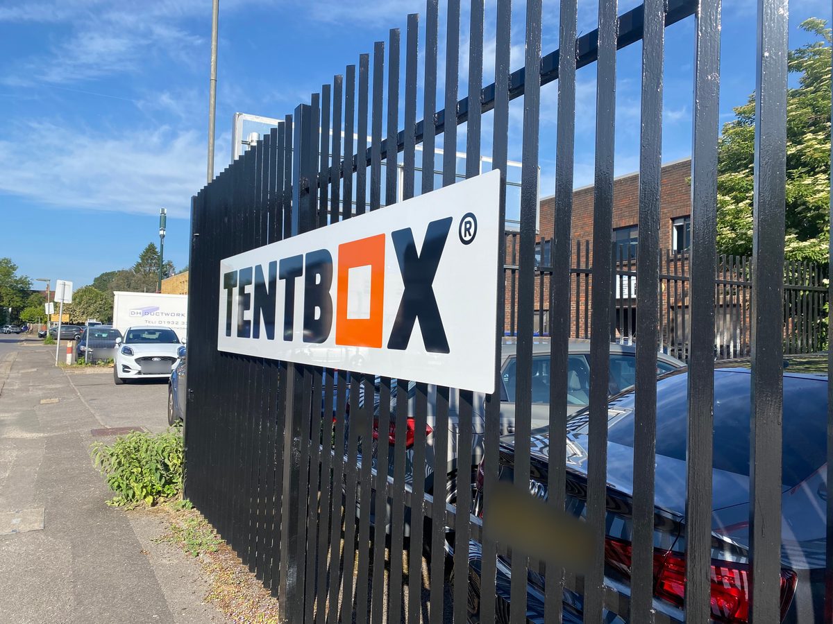 White Tentbox sign with black and orange logo fixed to black railings