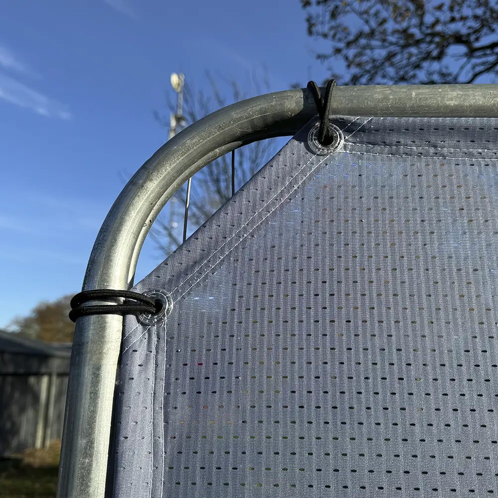 Mesh banner corner with reinforced eyelet tied to a metal frame with bungee cord