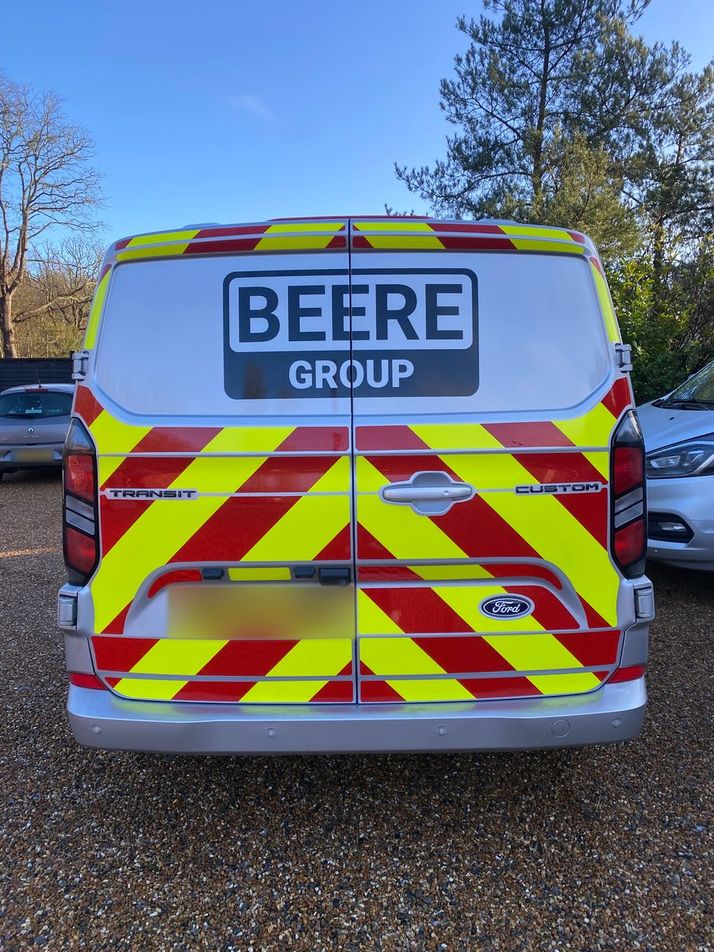 Rear of a white Ford Transit Custom with full red and yellow Chapter 8 chevrons and Beere Group logo