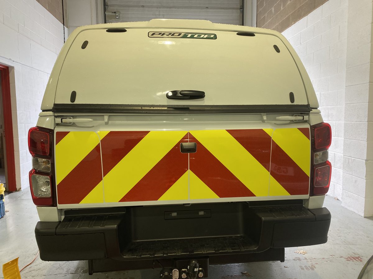 Rear of a white pickup with a red and yellow Chapter 8 chevron panel across the tailgate, in a workshop