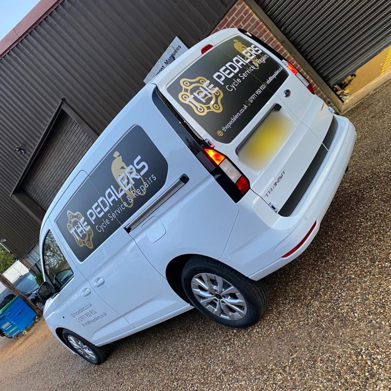 White Volkswagen Caddy with black and gold The Pedalers Cycle Service & Repairs graphics on the rear and side windows