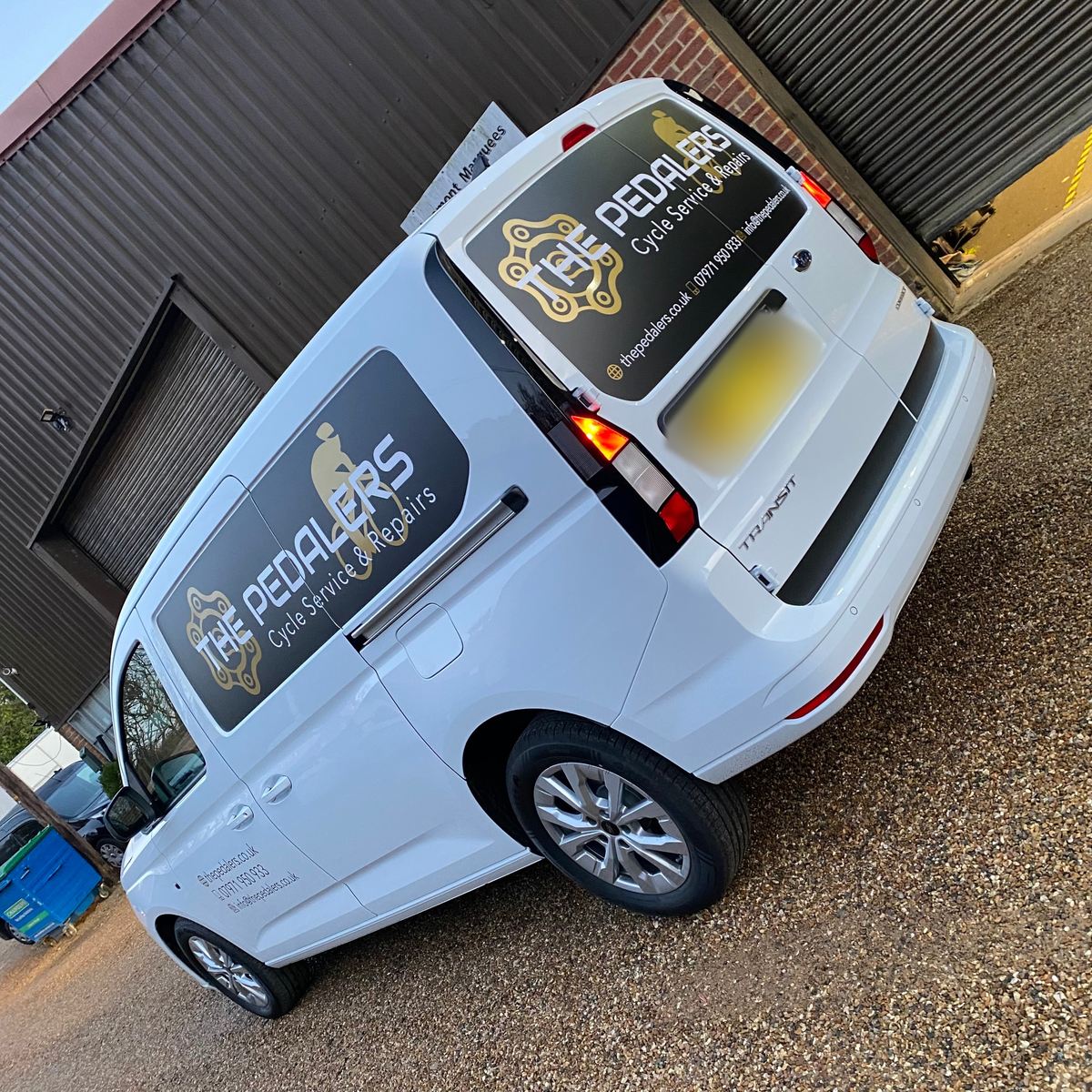 White Volkswagen Caddy with black and gold The Pedalers Cycle Service & Repairs graphics on the rear and side windows